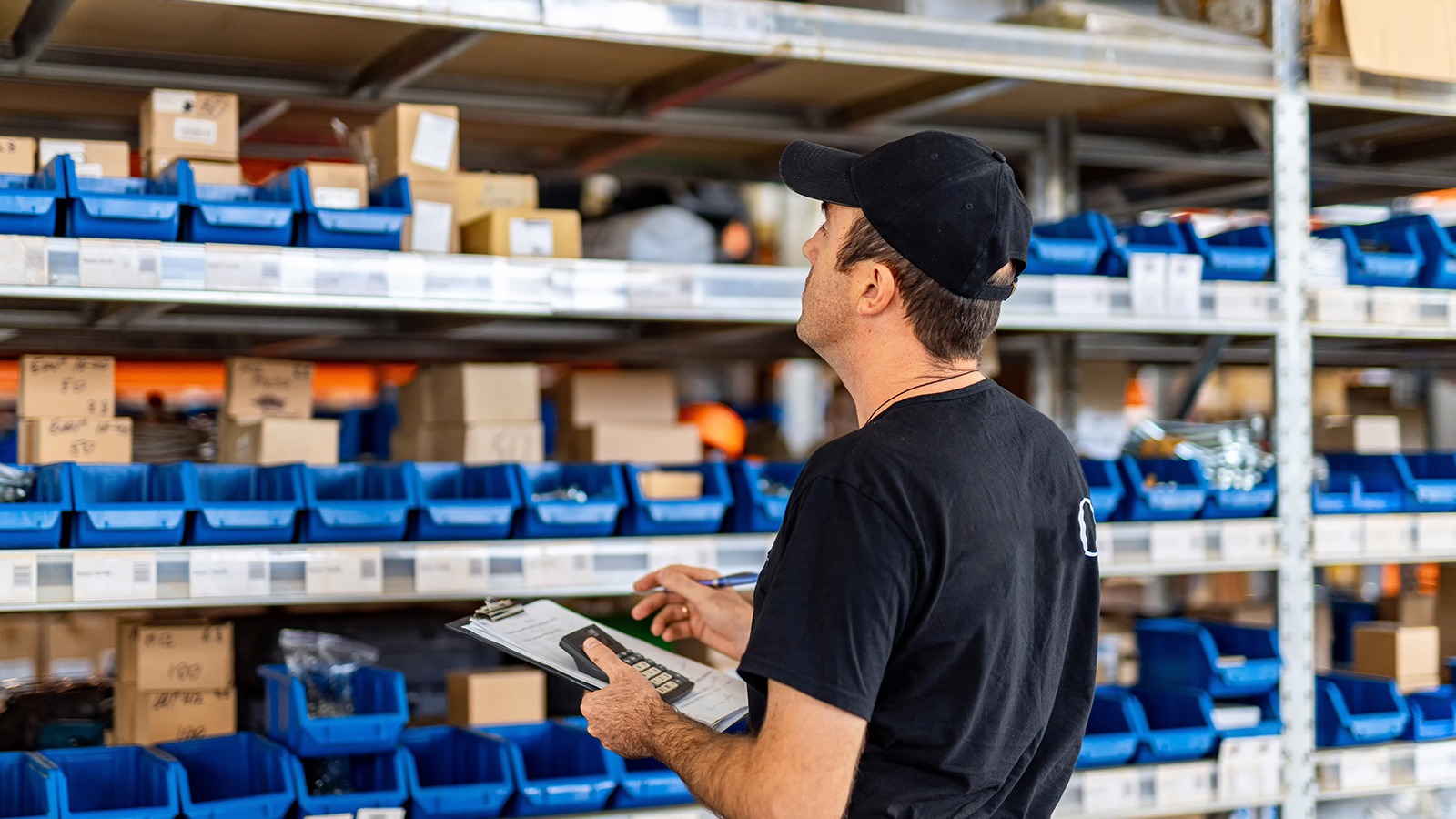 Arbeiter kontrolliert Lagerware im Regal mit Klemmbrett und Taschenrechner